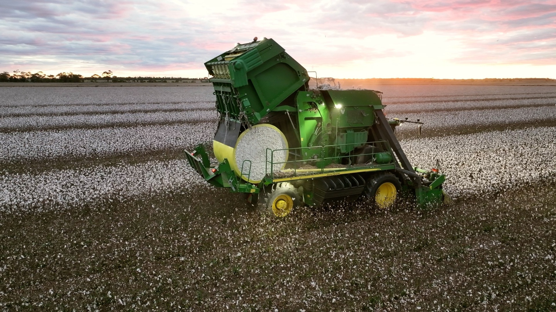Cotton picker dropping a bale, sun flare on horizon