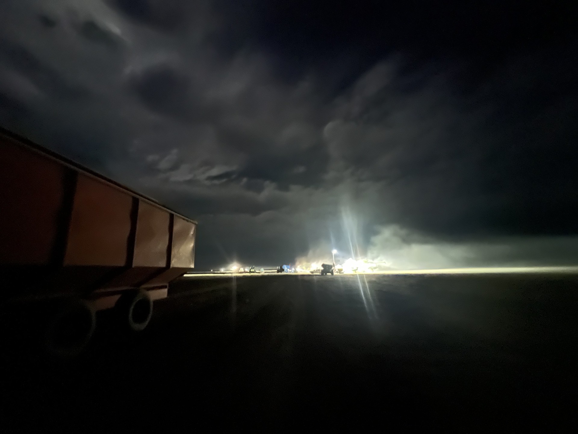 Grain header running under lights with storm clouds overhead